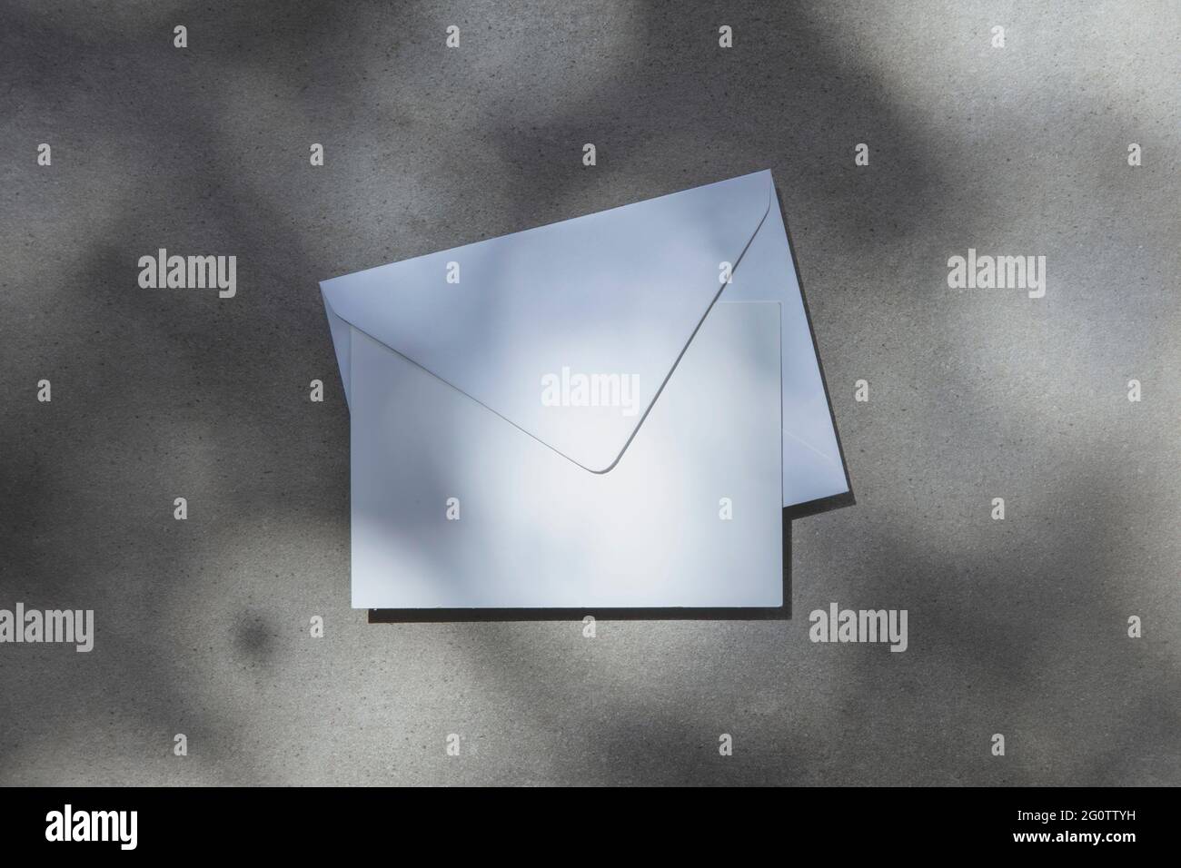 Weiße Einladungskarte oder Postkarte mit Umschlag unter strahlend hellem Sonnenlicht Stockfoto