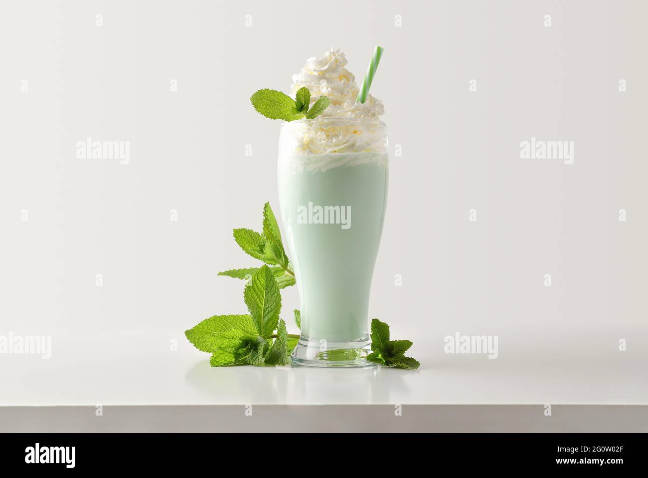 Minzmilchshake mit cremefarbenen Blättern auf weißem Holztisch und hellem, isolierten Hintergrund. Vorderansicht. Stockfoto
