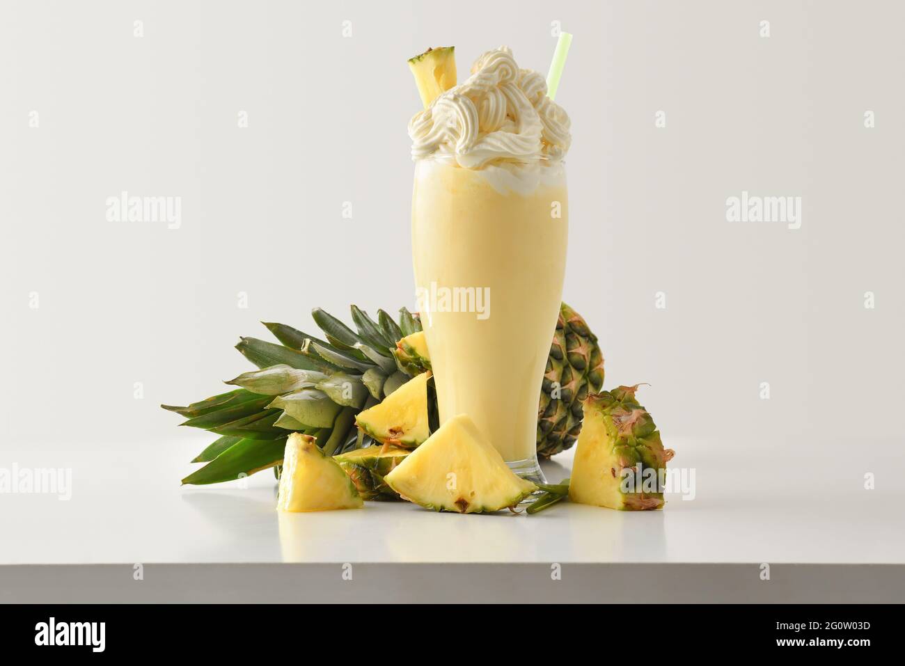 Ananas-Milchshake mit cremefarbener Dekoration, mit Früchten auf weißem Holztisch und hellem, isoliertem Hintergrund. Vorderansicht. Stockfoto
