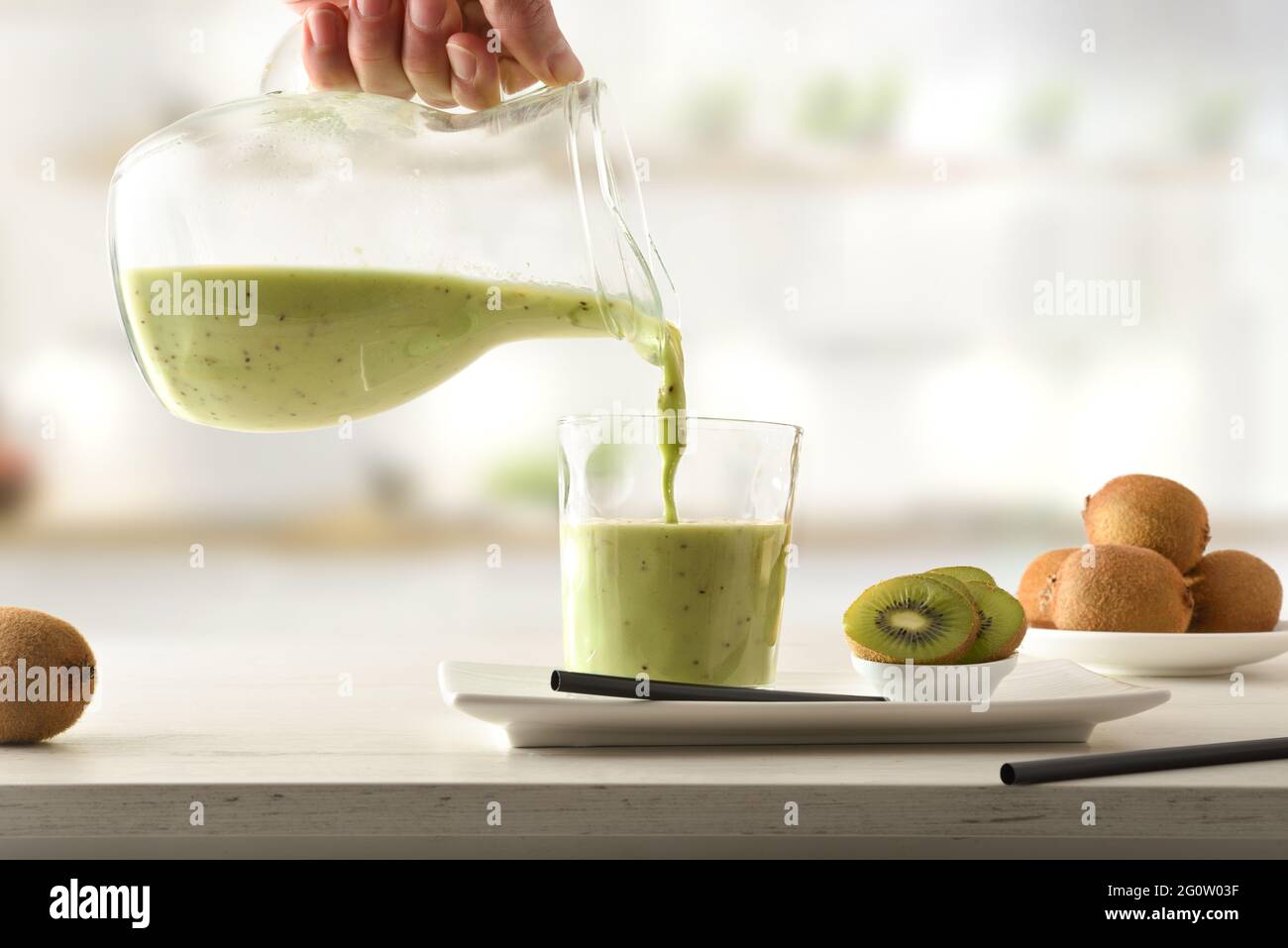 Person, die Kiwi trinkt, aus einem Krug mit geschnittenem Obst in Behältern auf der Küchenbank. Vorderansicht. Stockfoto