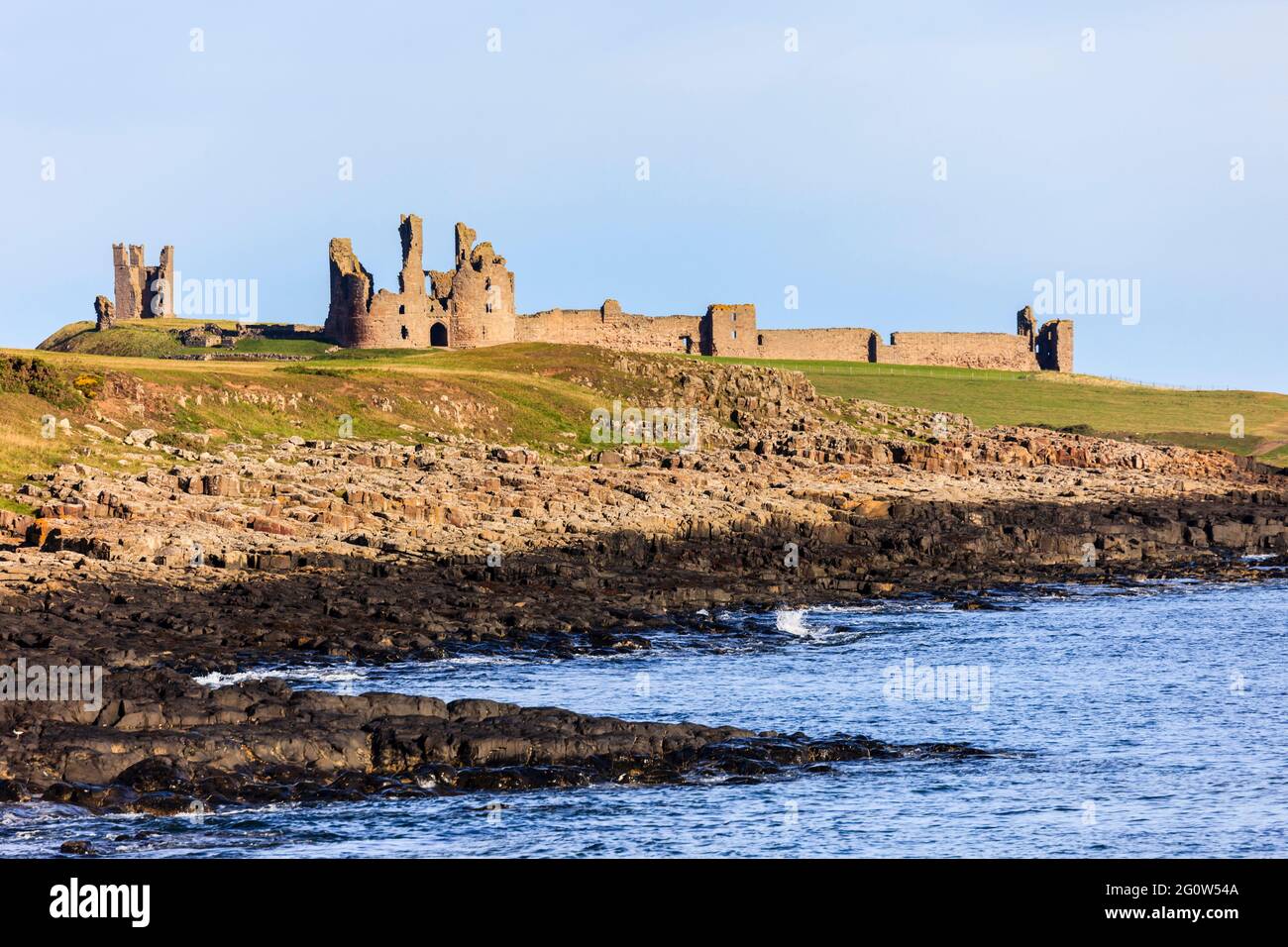 Blick über das Meer auf die Burgruinen von Dunstanburgh an der felsigen Nordostküste. Craster, Northumberland, England, Großbritannien Stockfoto