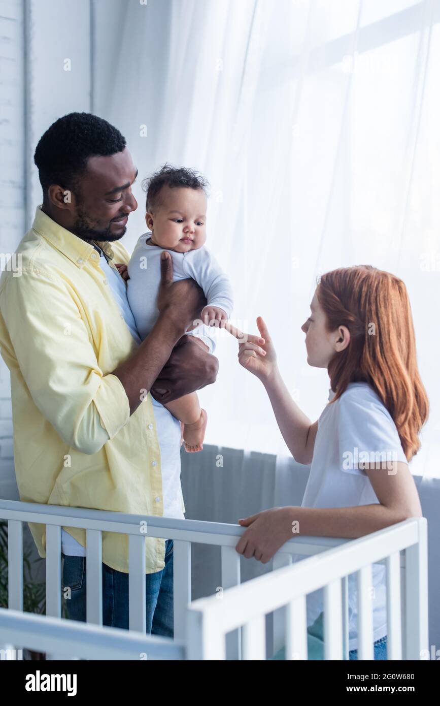 Präteen Mädchen berühren Hand von Kleinkind Schwester in der Nähe lächelnd afroamerikanischen Vater Stockfoto