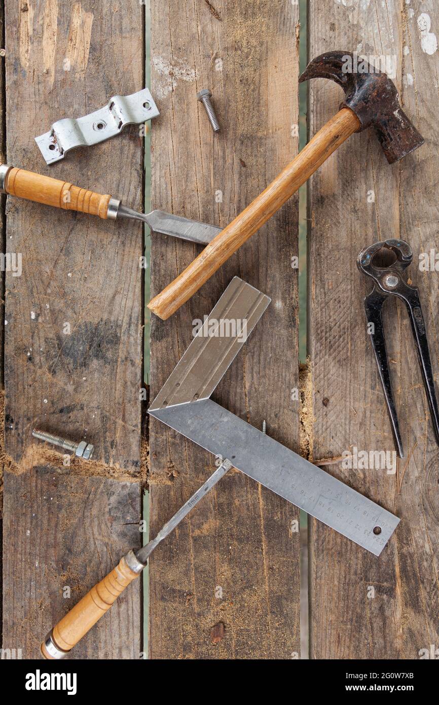 Einige Tischlerwerkzeuge auf einem Holztisch. Es gibt einen Hammer, eine Zange, zwei Meißel, ein Quadrat und Schrauben Stockfoto