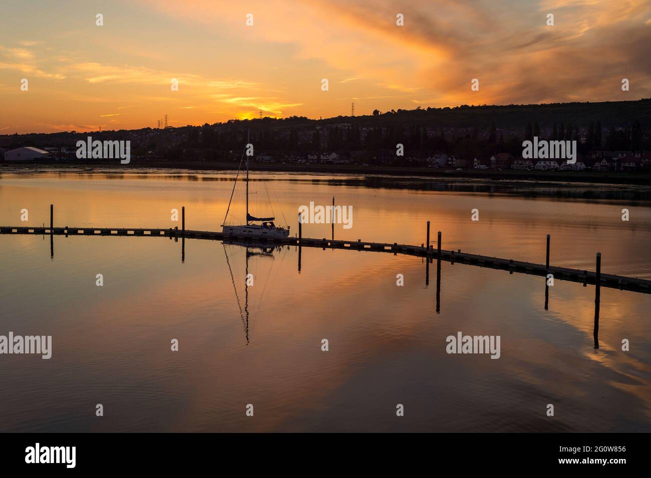Segelyacht, die bei Sonnenuntergang in einem ruhigen Hafen auf einem Ponton festgemacht ist. Stockfoto