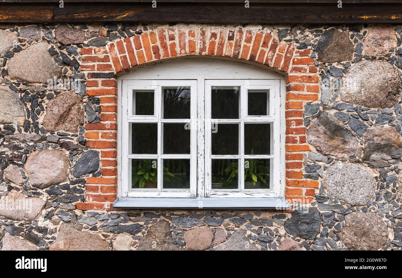 Fenster mit weißem Holzrahmen in einer Steinmauer mit Ziegelbogen Stockfoto