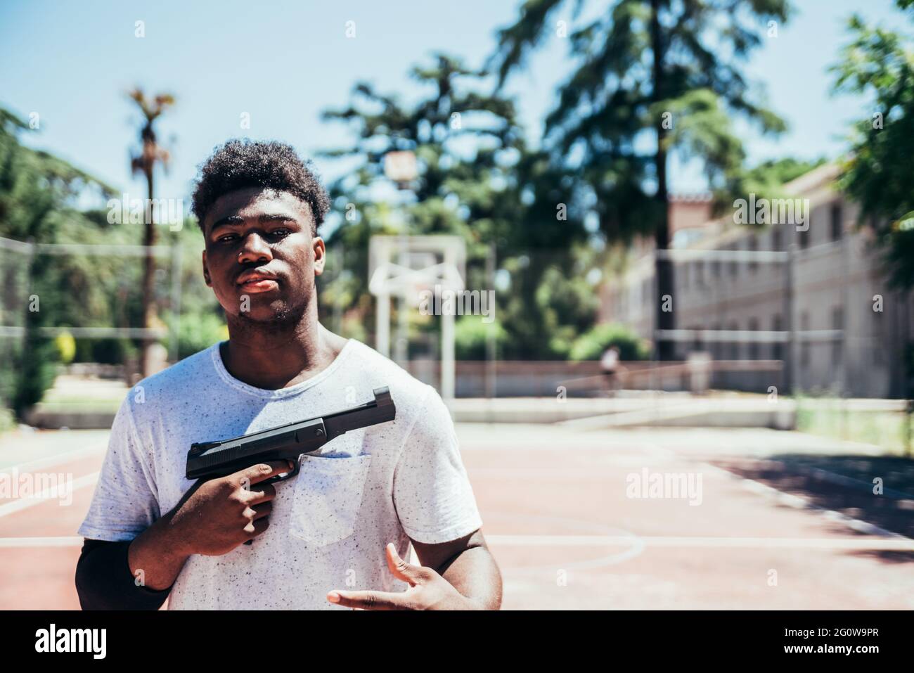 Schwarzer afroamerikanischer Junge, der eine Waffe auf einem städtischen Basketballplatz hält. Stockfoto