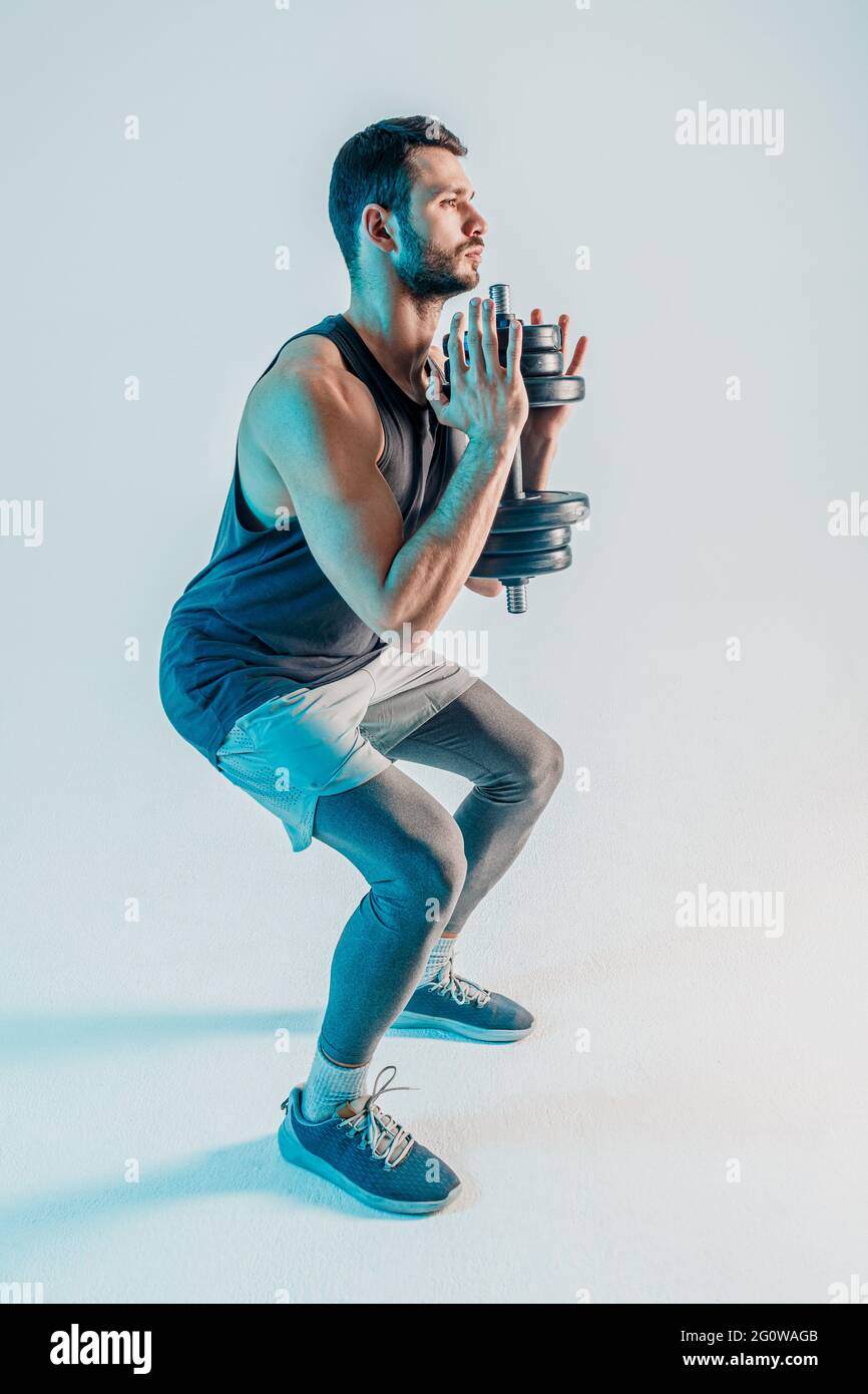 Konzentrierter junger Mann sitzt mit Hanteln auf Stockfoto