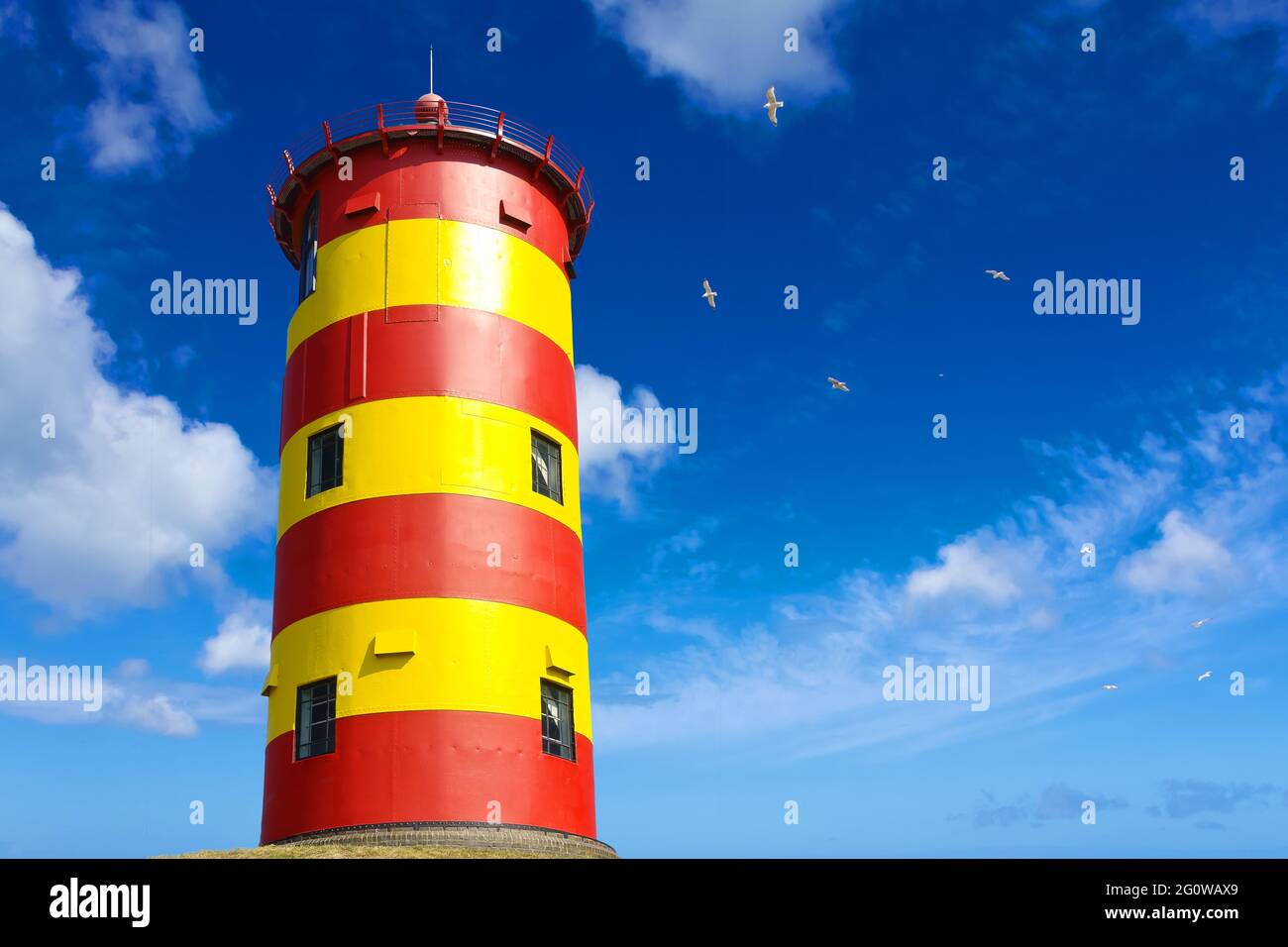 Berühmter gelb-rot gestreifter Leuchtturm Pilsum bei Greetsiel, Ostfriesland, Nordsee, Deutschland, gegen einen blauen Himmel. Stockfoto