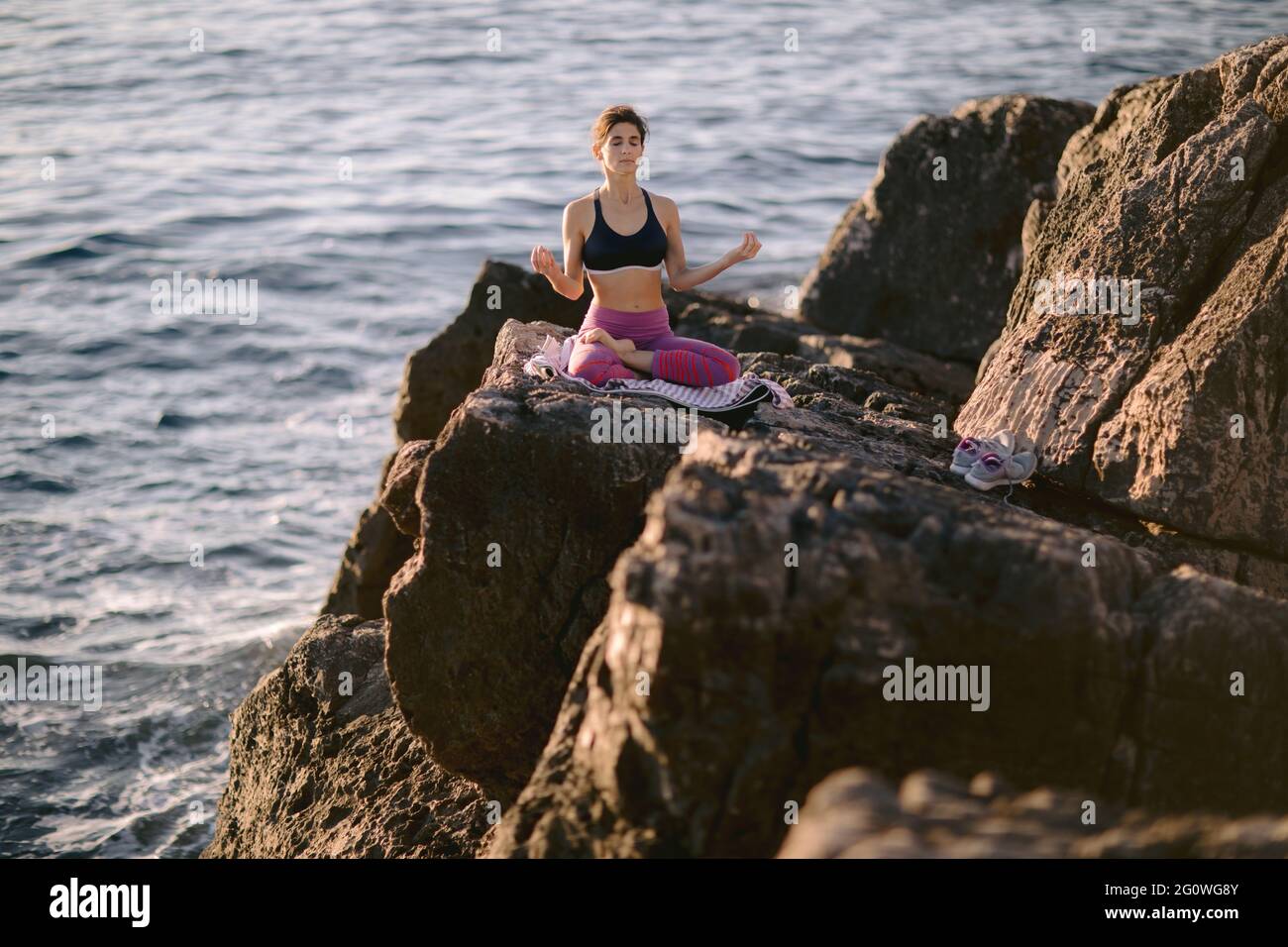 Schöne junge Frau, die Meditation auf der Klippe in der Nähe des Meeres macht. Yoga und Bewegungskonzept in der Natur. Stockfoto