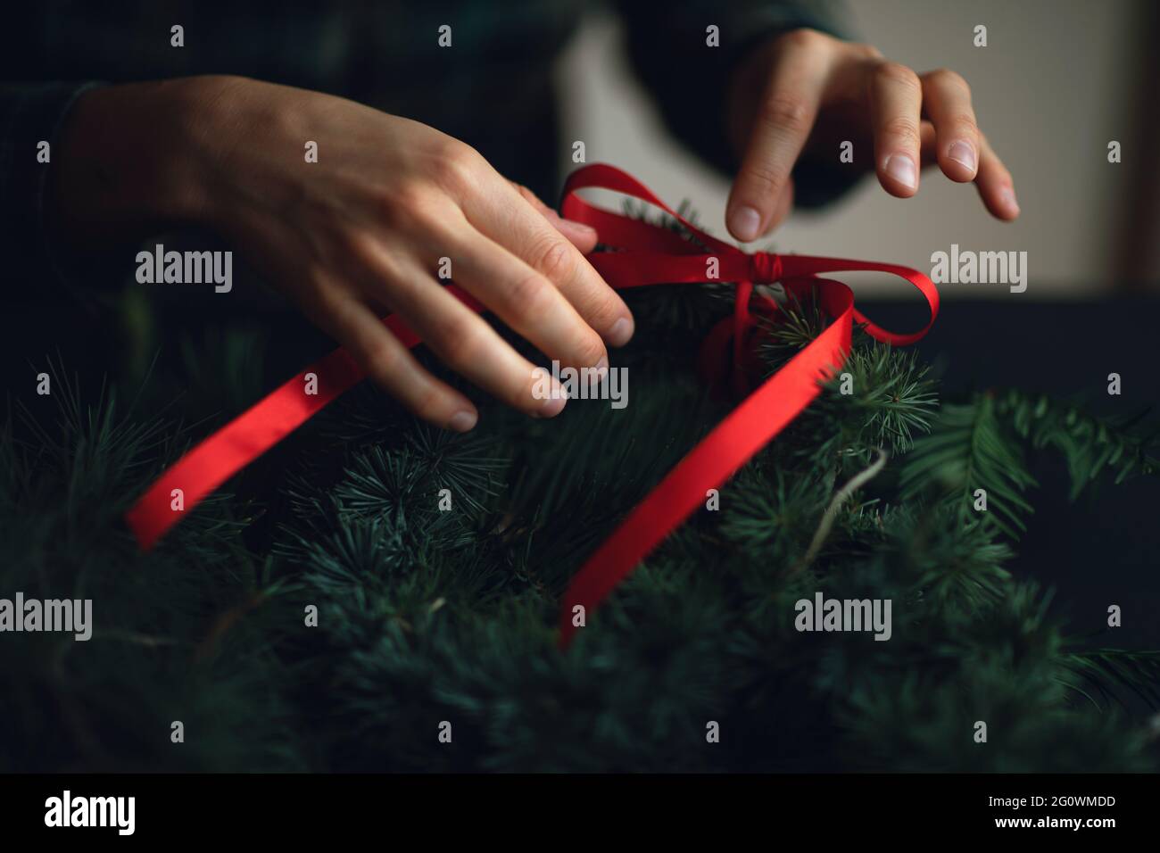 Frau, die einen weihnachtskranz mit Kiefern und rotem Band macht. Ideen für die weihnachtsdekoration. Weihnachten Hintergrund. Stockfoto