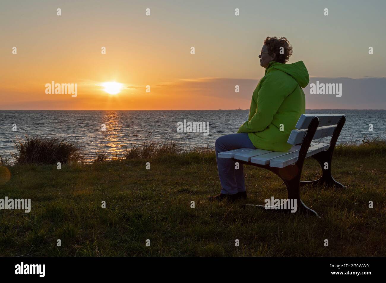 Frau, die den Sonnenuntergang auf einer Bank genießt, West Beach, Großenbrode, Schleswig-Holstein, Deutschland Stockfoto