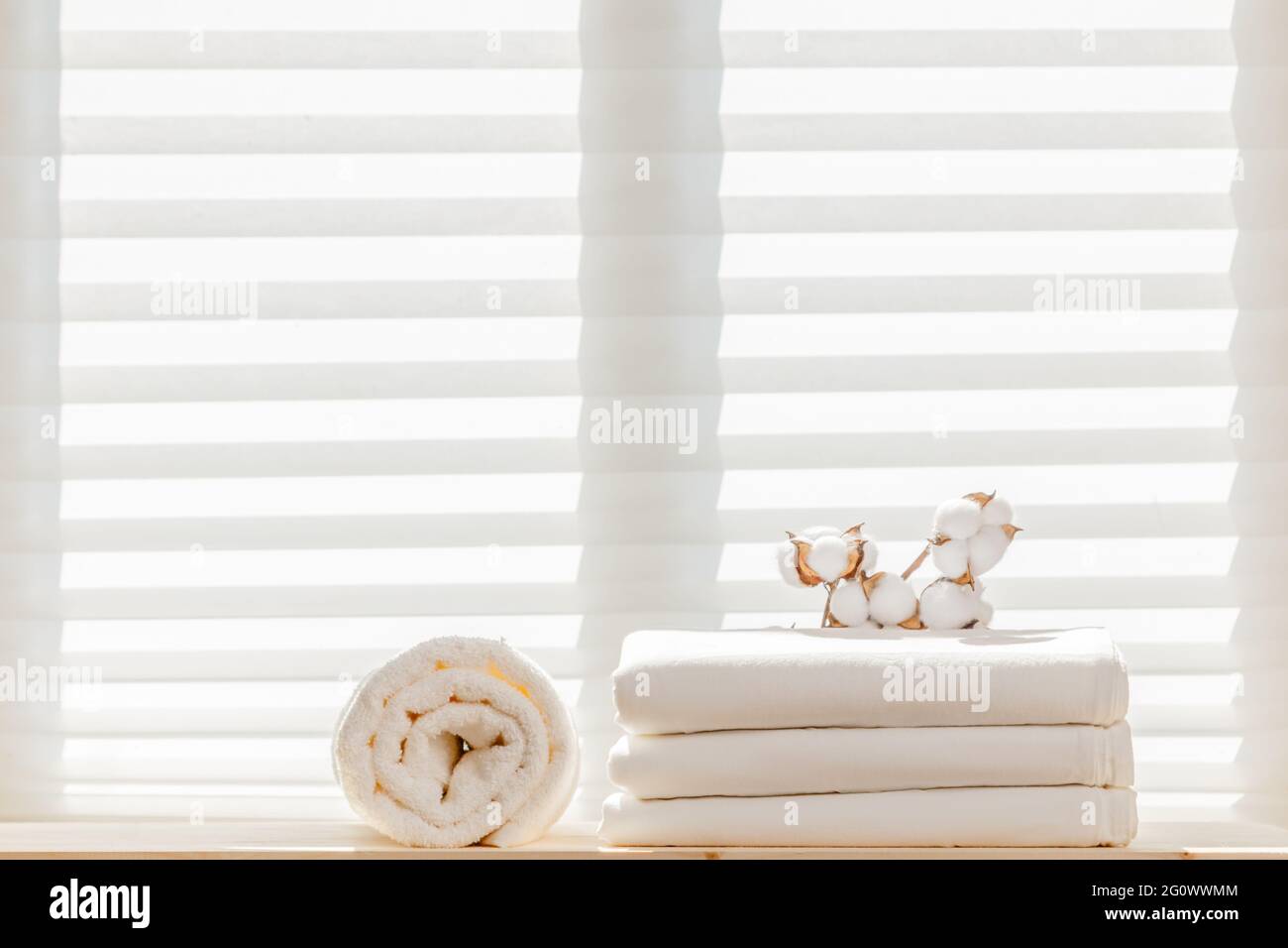 Weiße Bettwäsche Bettwäsche Bettwäsche mit einem Baumwollzweig und einem Frottee-Handtuch vor dem Hintergrund des Fensters. Natürliche Zusammensetzung. Stockfoto