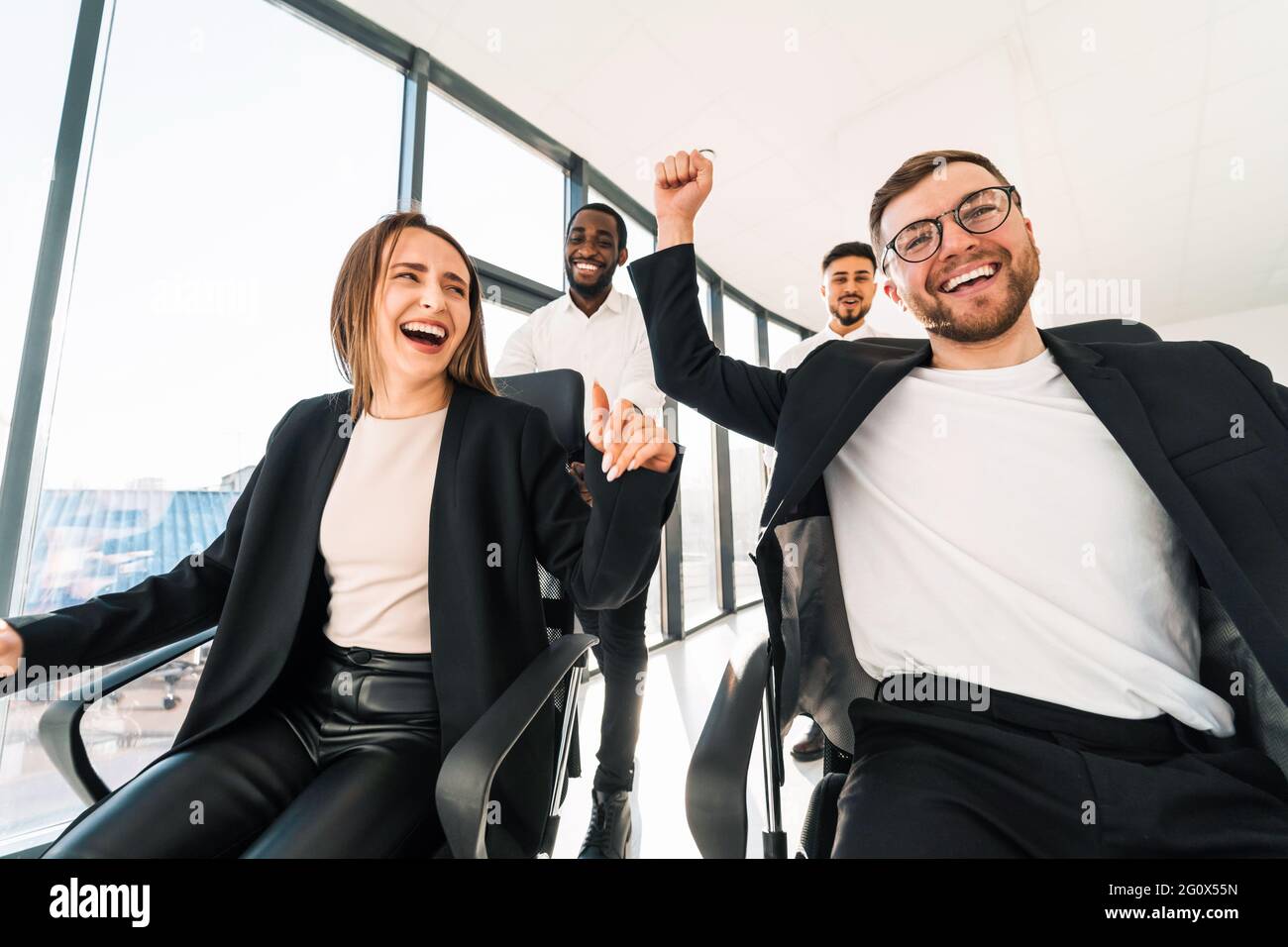 Fröhliche Mitarbeiter fahren auf Stühlen um das Büro und feiern das Ende der Arbeitswoche Stockfoto