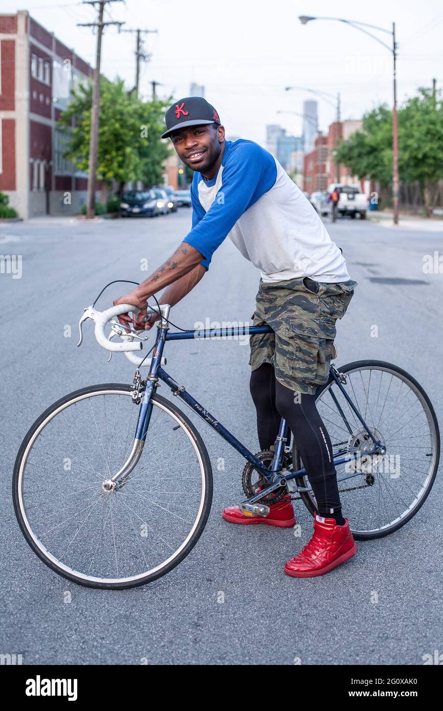 Junger Afroamerikaner mit Fahrrad, das draußen auf der Straße mit städtischem Hintergrund in Chicago, IL, USA steht. Stockfoto