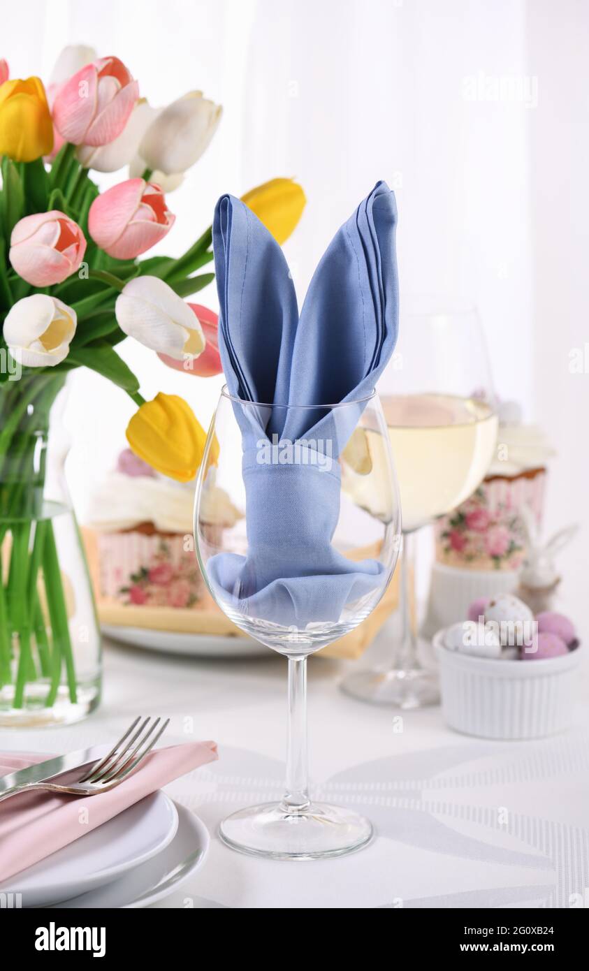 Eine Serviette, die in Form von Hasenohren in einem Glas gefaltet ist, das Konzept, zu Ehren von Ostern einen festlichen Tisch zu legen. Stockfoto