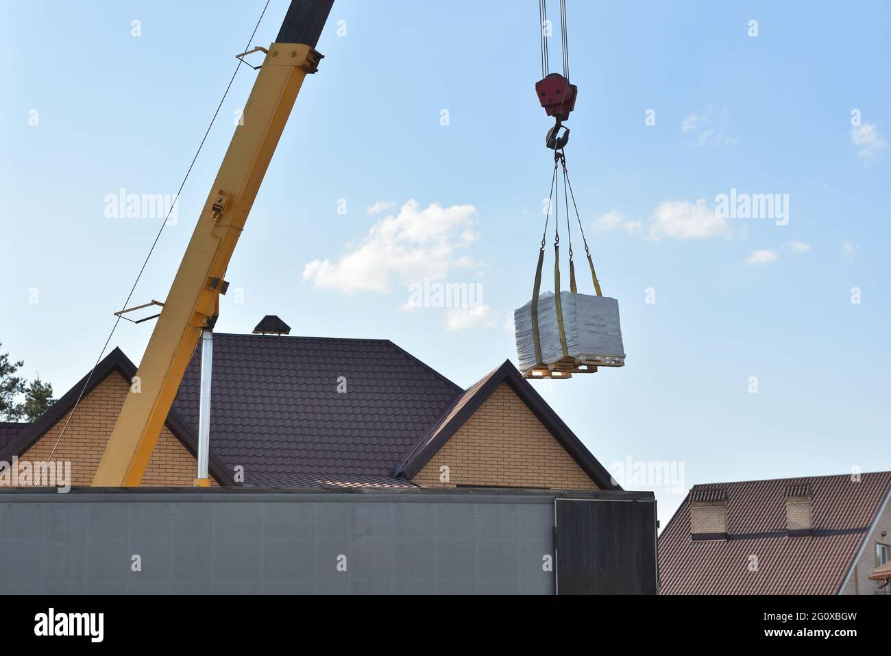 LKW-Kran hebt Baustoffe auf dem Hintergrund eines Privathauses Stockfoto