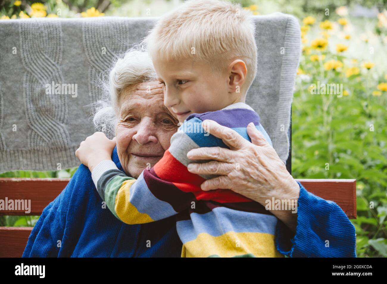 90-jährige ältere Frau Ur-Großmutter umarmt Ur-Enkel. Kind Junge Unterstützung und Blumen zu Ur-Großmutter. Familiengruppe, Unterstützung Stockfoto