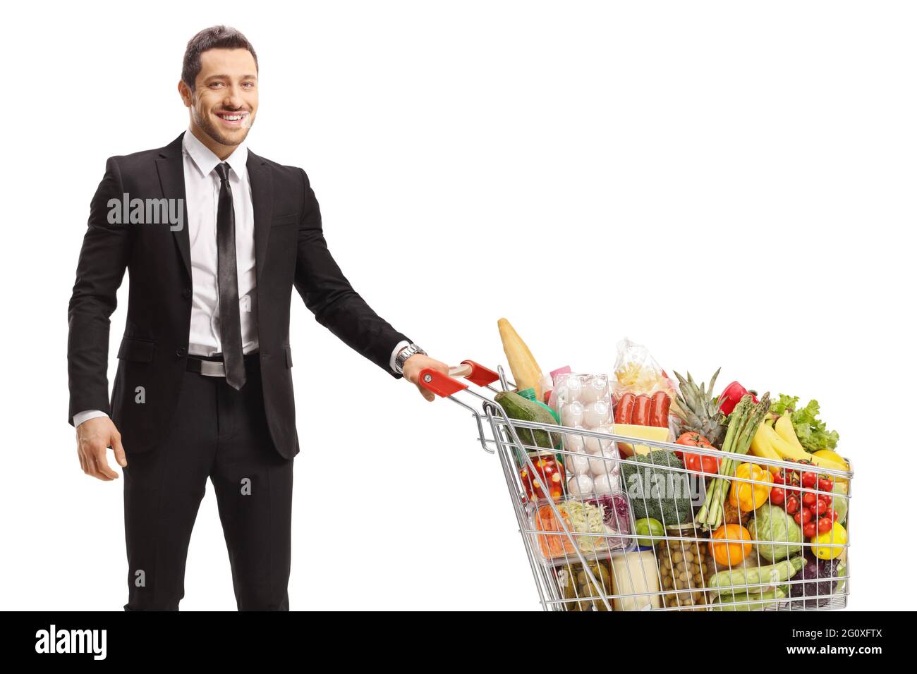 Junger Geschäftsmann posiert mit einem Einkaufswagen mit Essen isoliert auf weißem Hintergrund Stockfoto