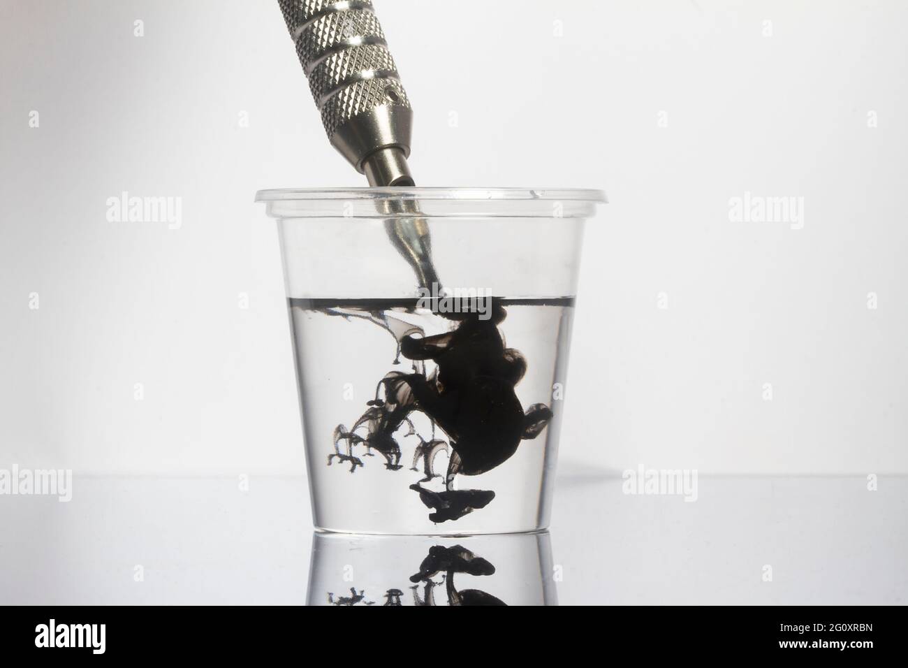 Tattoo Maschine schwarze Tintennadeln mit sauberem Wasser in klarem Glas reinigen Stockfoto