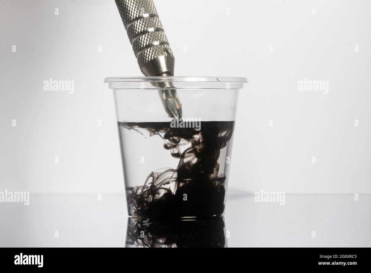 Tattoo Maschine schwarze Tintennadeln mit sauberem Wasser in klarem Glas reinigen Stockfoto
