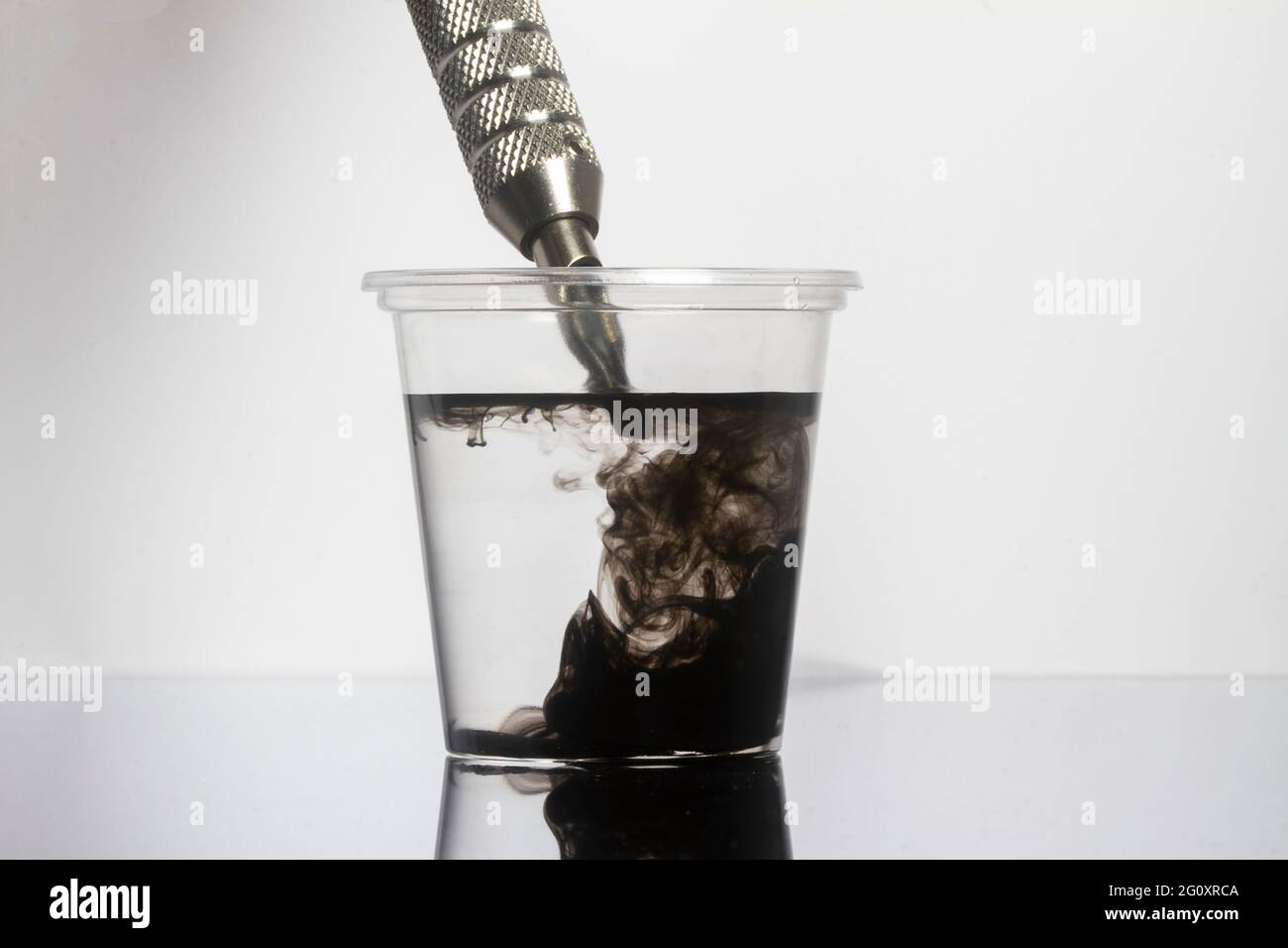 Tattoo Maschine schwarze Tintennadeln mit sauberem Wasser in klarem Glas reinigen Stockfoto