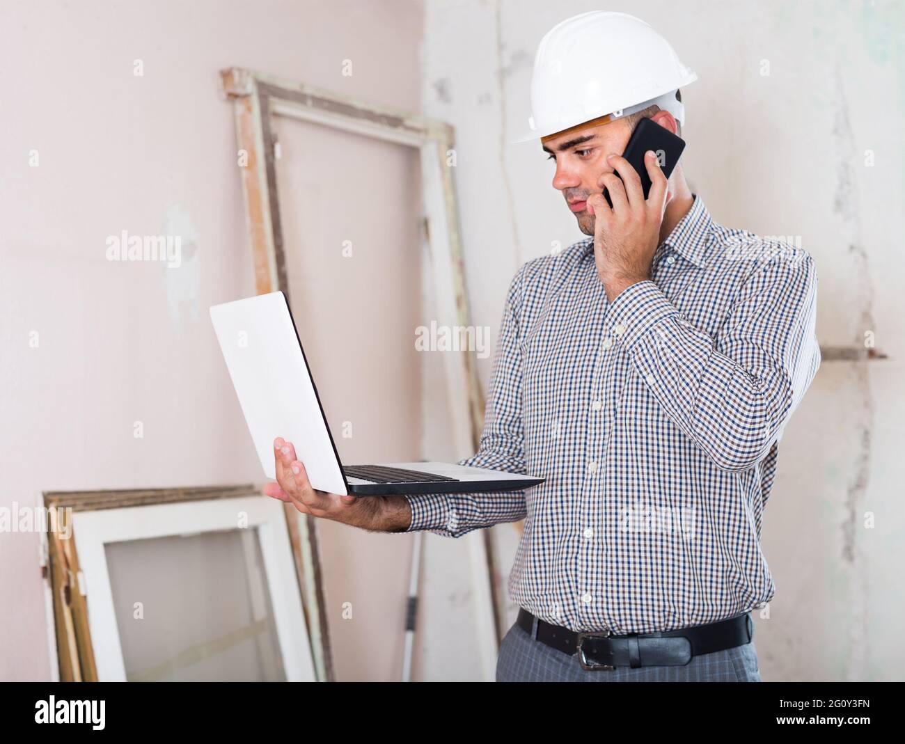 Junge Architektin im Gespräch auf dem Handy mit Laptop in der Hand Stockfoto