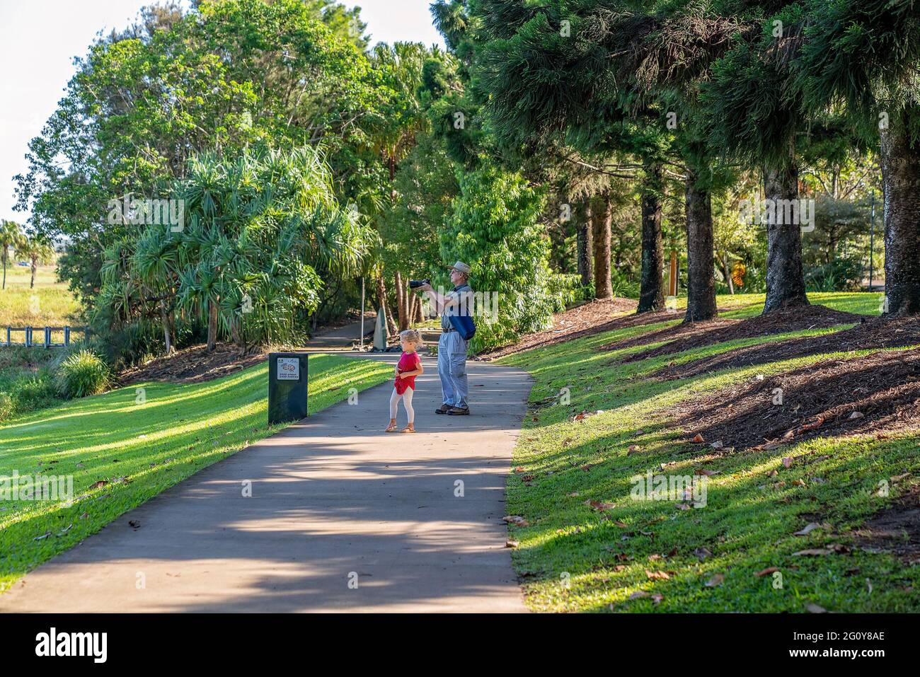 Mackay, Queensland, Australien - 2021. Juni: Ein kleines Kind steht neben ihrem Großvater, als er in den botanischen Gärten ein Foto macht Stockfoto