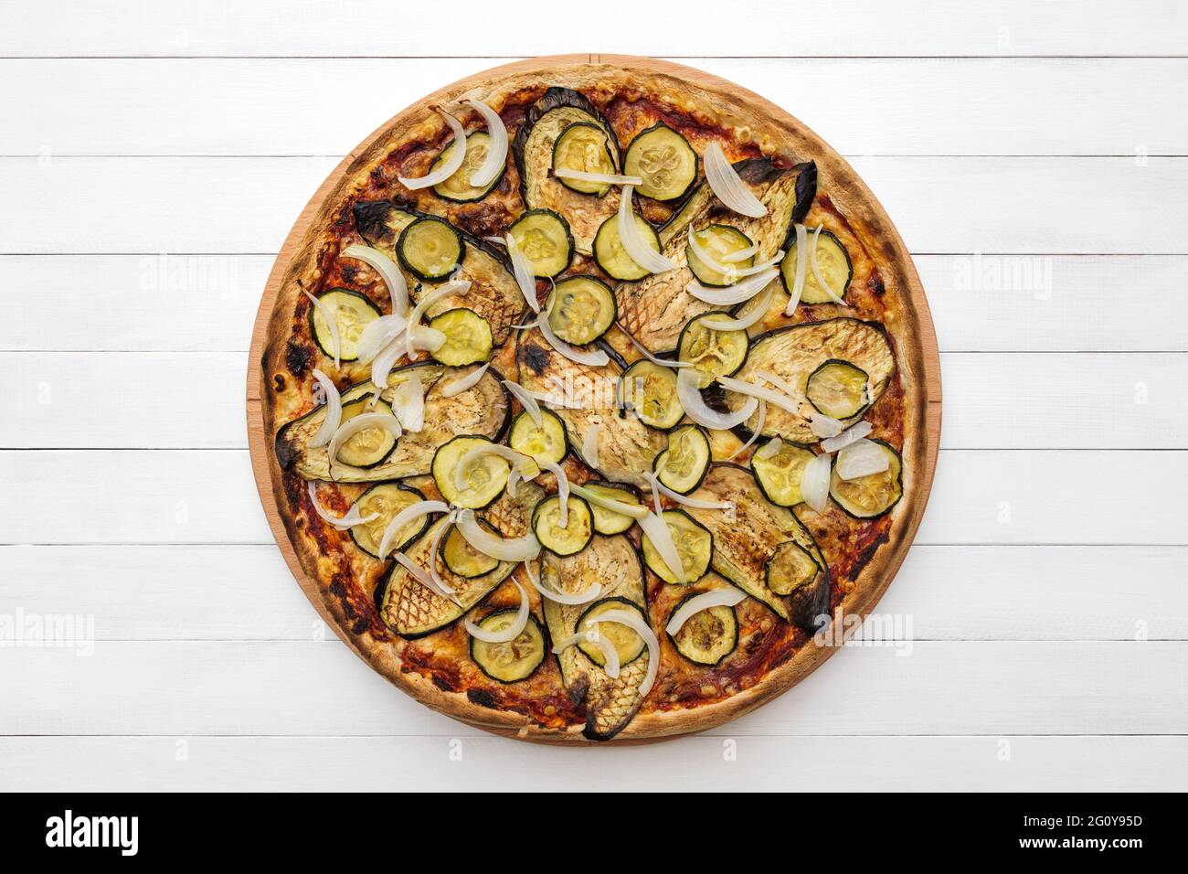 Ganze vegetarische Pizza mit gegrillter Aubergine, Zucchini und Zwiebeln, auf Holzplatte gekrönt. Draufsicht auf Whiteboard-Hintergrund Stockfoto