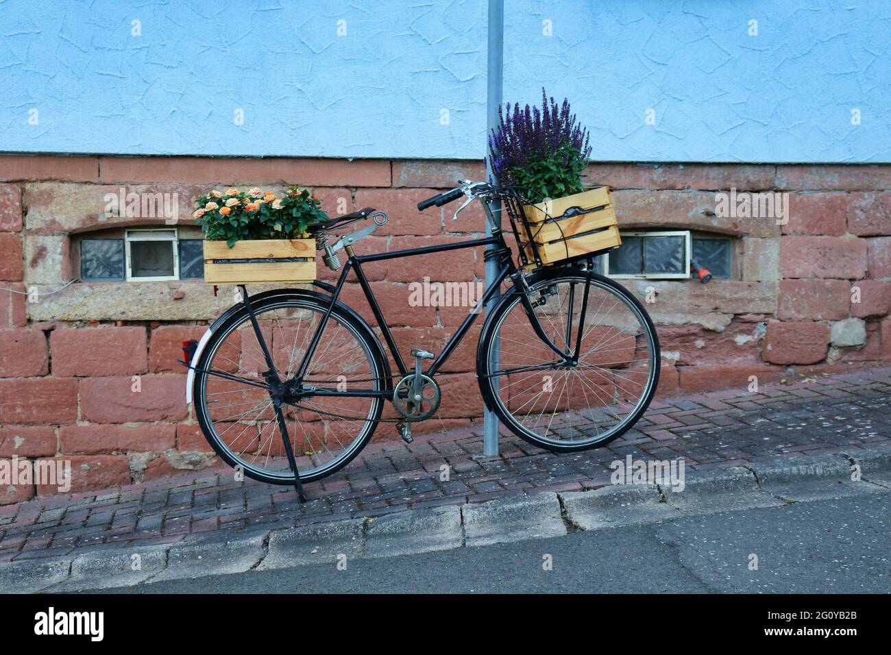 Fahrrad mit Blumen, die in Blumenksten wachsen, die an einer Stange auf  einem Brgersteig vor einem Haus in einem deutschen Dorf befestigt sind  Stockfotografie - Alamy