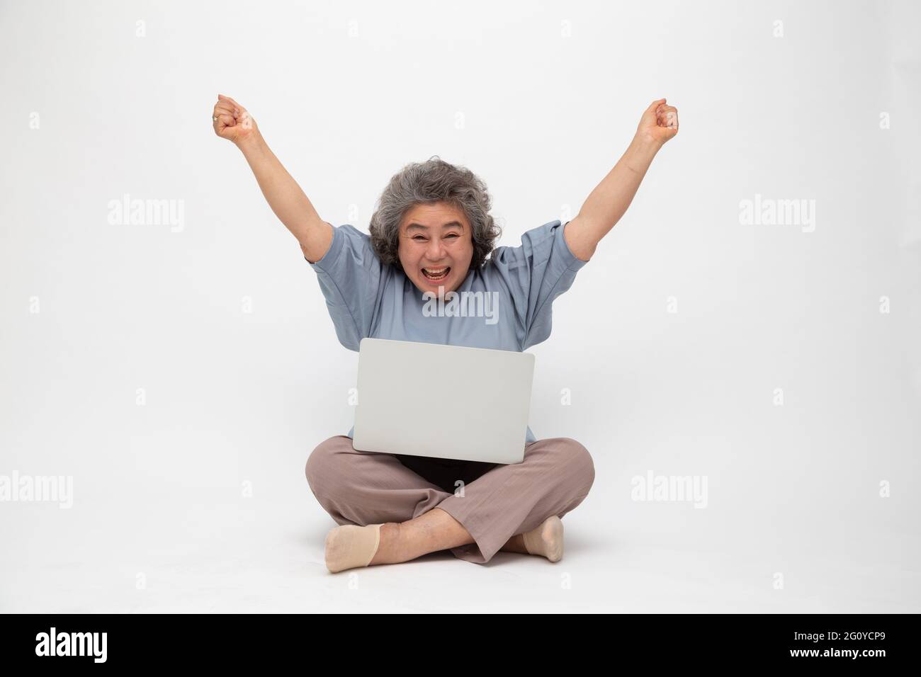 Aufgeregt Senior asiatische Frau Gefühl Gewinner feiern Sieg Online-Geschäftserfolg und sitzen auf dem Boden mit Laptop isoliert auf weißem Hintergrund, F Stockfoto