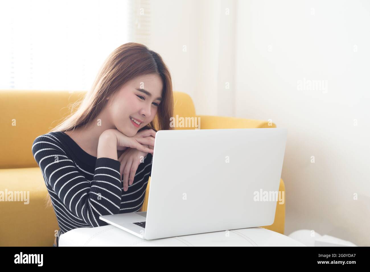 Lächelnde junge asiatische Frau mit Laptop und Videokonferenz im Wohnzimmer, niedlich schüchtern Frauen in Valentines Tag Konzept zu Freund Stockfoto