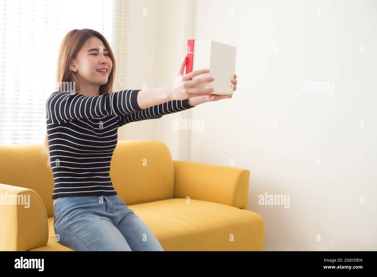 Gerne schöne asiatische Frau lächeln mit roter Geschenkbox und kopieren Raum weiß Wohnzimmer Hintergrund. Junge Mädchen in Liebe, Geschenke von Liebhaber. N Stockfoto