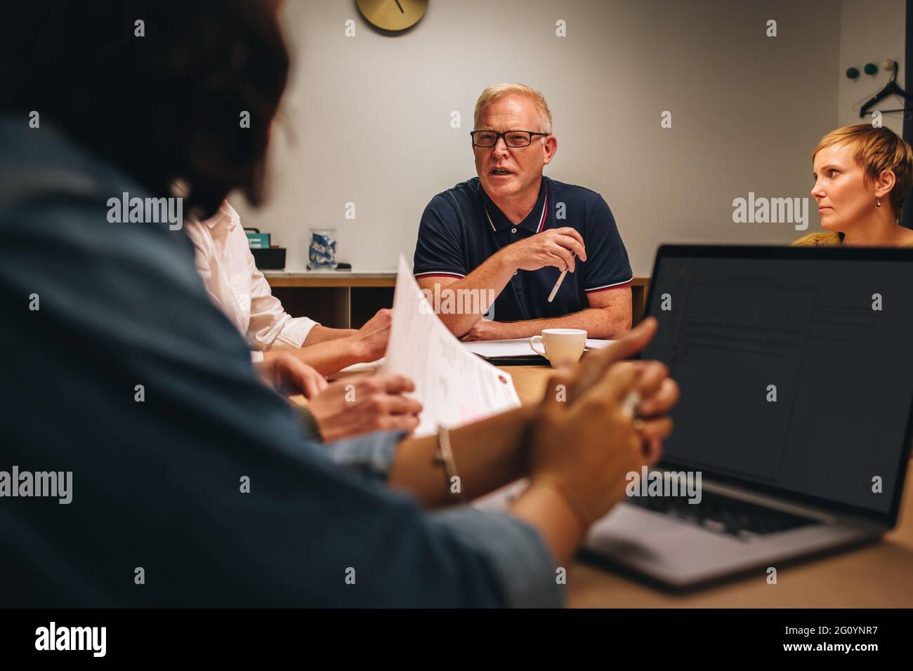 Senior-Mann im Gespräch mit Kollegen im Konferenzraum. Ein reifer Geschäftsmann mit Führungskräften, die im Vorstandszimmer sitzen und eine Strategie planen. Stockfoto