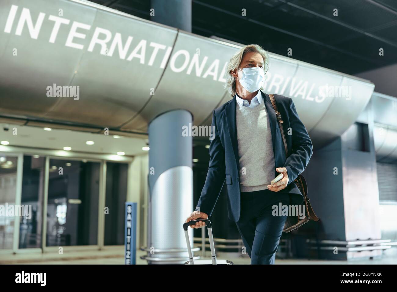 Geschäftsmann, der eine Gesichtsmaske mit Gepäck trägt, läuft im Flughafenterminal. Mann, der während des Coronavirus-Ausbruchs reist. Stockfoto