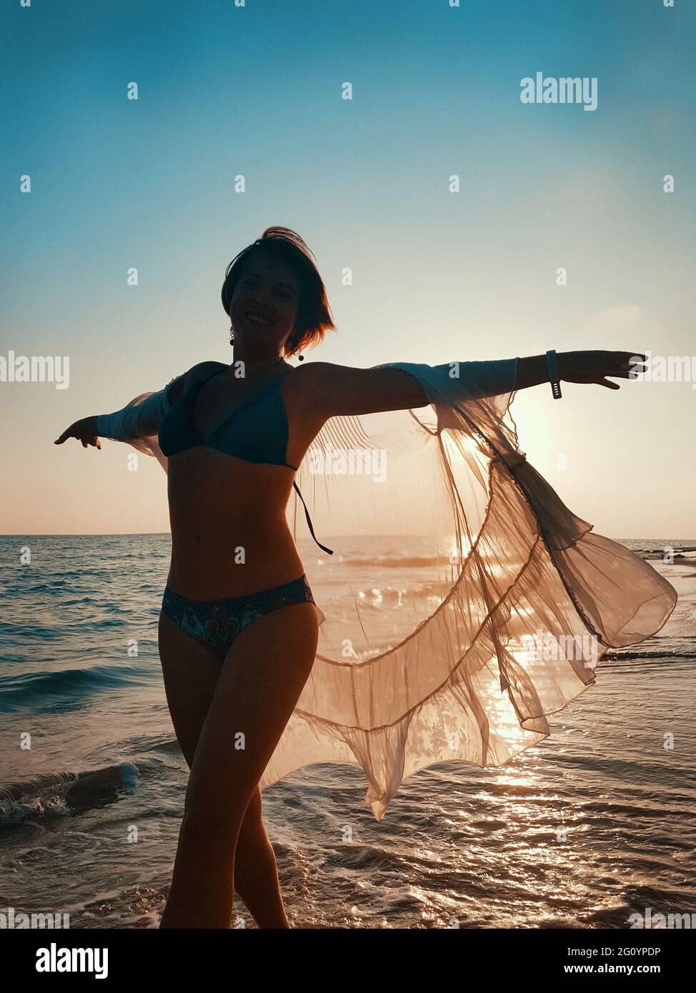 Junge Frau in weiß vertuschen tanzen am Strand bei Sonnenuntergang Stockfoto