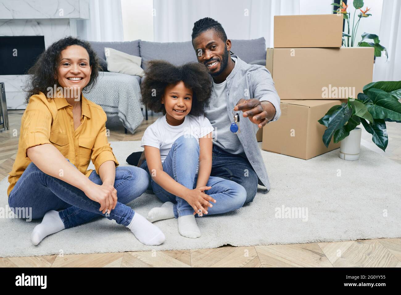 Afroamerikanische Familie zieht in ein neues Zuhause. Vater, Mutter und Tochter sitzen nach dem Auspacken glücklich auf dem Boden des Hauses. Kauf oder renti Stockfoto