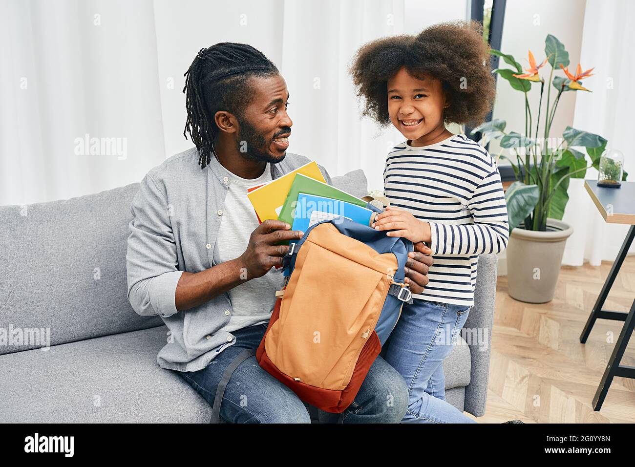 Vatertag. Vater hilft Tochter, farbige Copybooks vor ihrem ersten Schultag in die Schultasche zu legen. Glückliche Vaterschaft Stockfoto