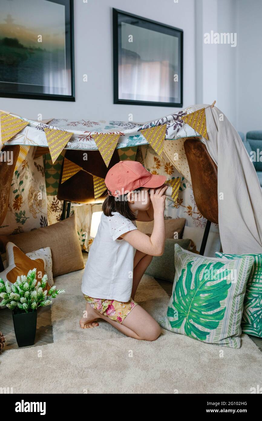 Kleines Mädchen, das mit einem Fernglas aus Pappe spielt, während es zu Hause im Wohnzimmer campt Stockfoto
