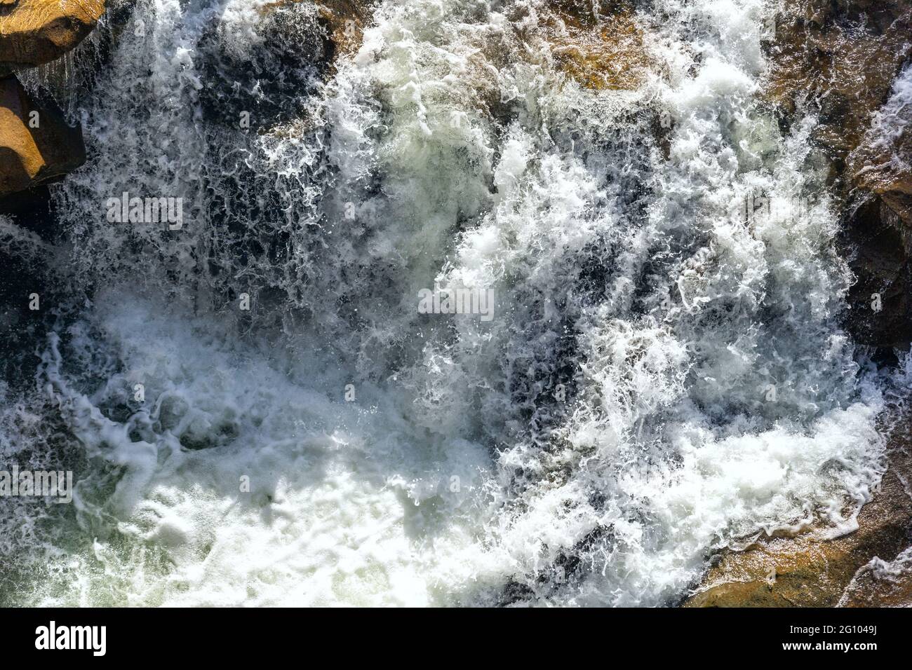 Nahaufnahme der abstrakten Textur über dem Blick auf den Flusslauf und klares, frisches kaltes Wasser, das durch Bergfelsen im Tal mit Schaum und Blasen fließt Stockfoto