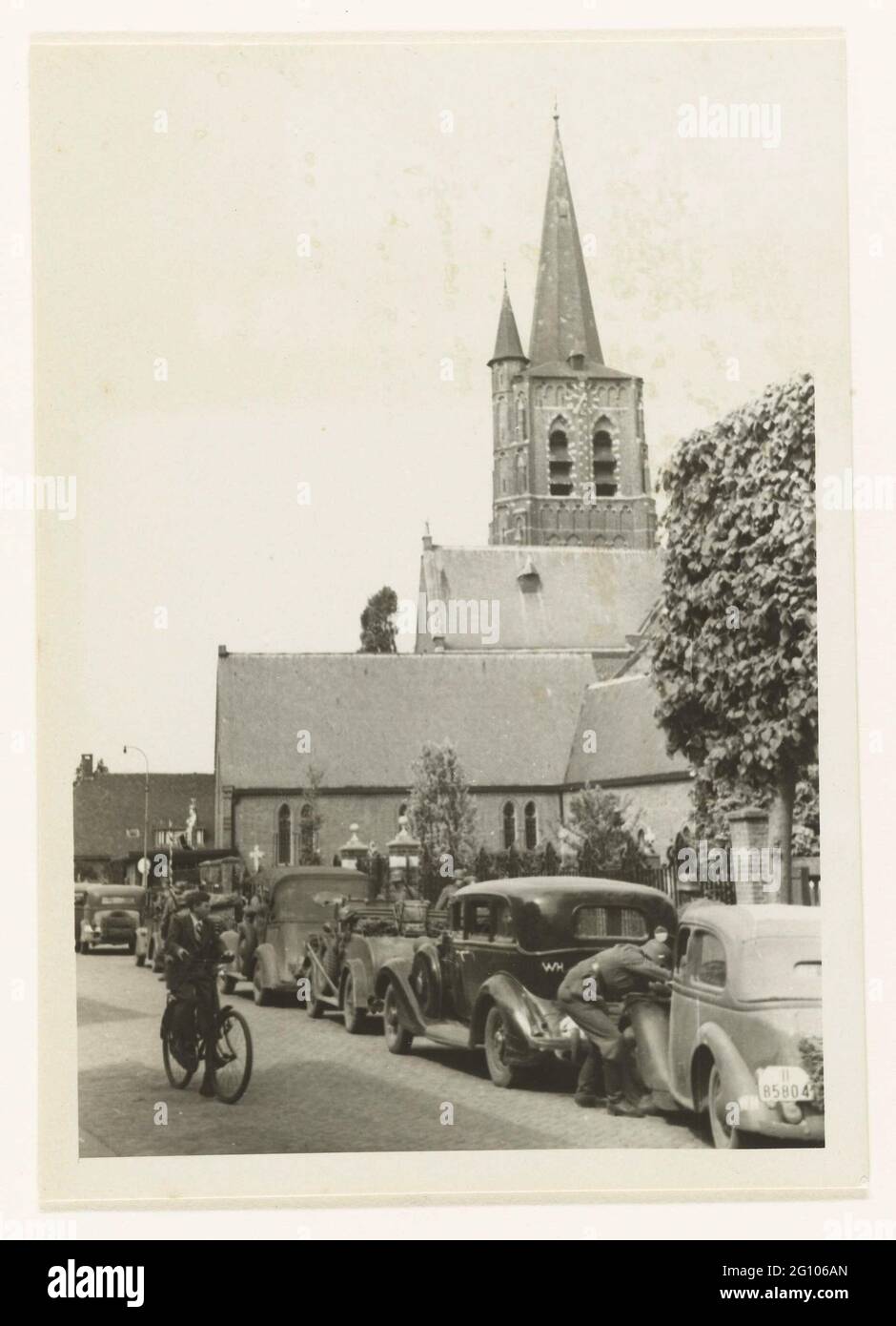 Die Wehrmacht in Loon op Zand. Die Wehrmacht wird in einer Straße mit mehreren Autos geparkt, dahinter befindet sich die Kirche. Ein Radfahrer auf der linken Seite. Rechts davon: Loon op Zand Stockfoto