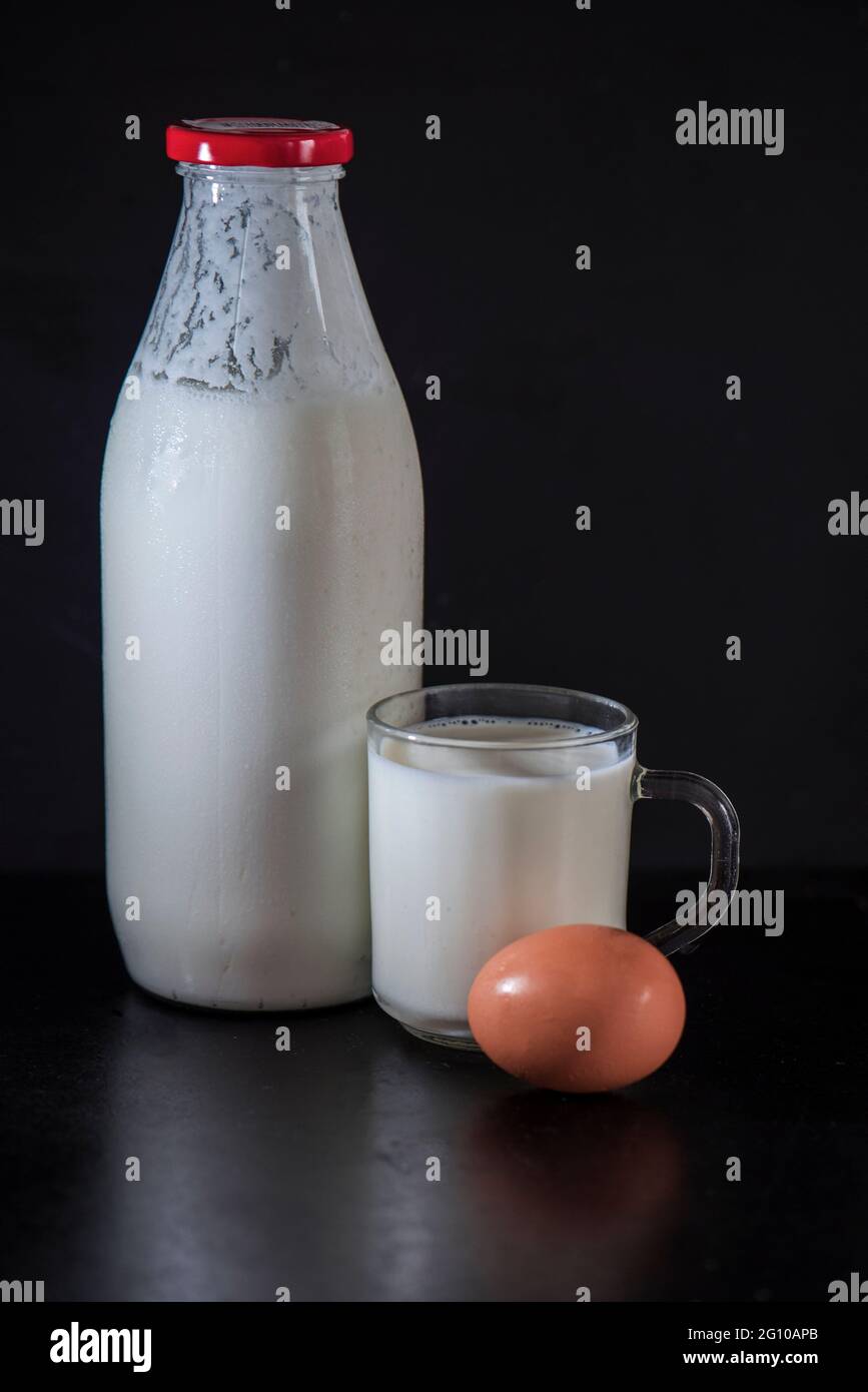 Ein saures Getränk aus fermentierter Milch namens Kefir in einer Flasche mit einer Tasse Kefir und einem Bio-Ei auf schwarzem Hintergrund, aus der Nähe, isoliert Stockfoto