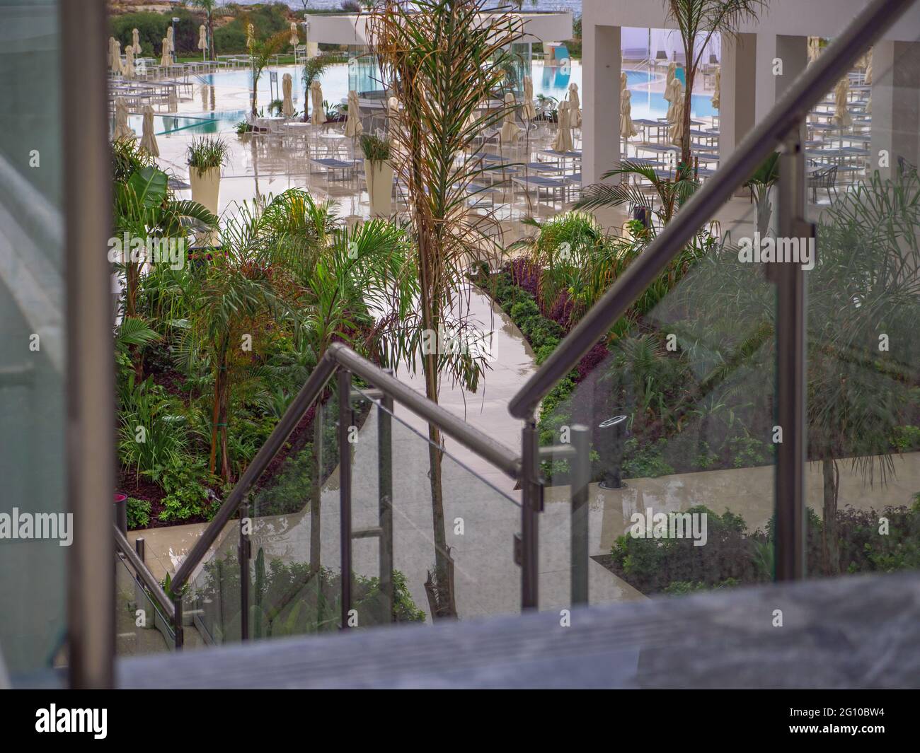 Blick unten auf einen Hotelhof mit Swimmingpool, Sonnenliegen, Sonnenschirmen und Grün an einem üblen Regentag in Napa, Zypern. Einsames Hotel. Stockfoto