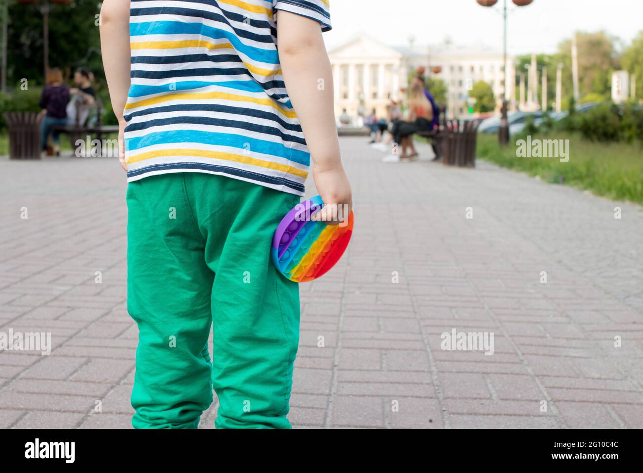 Ein kleines Kind hält ein Spielzeug Antistress Pop es mit einem Platz für Text im Hintergrund des Stadtparks. Stockfoto