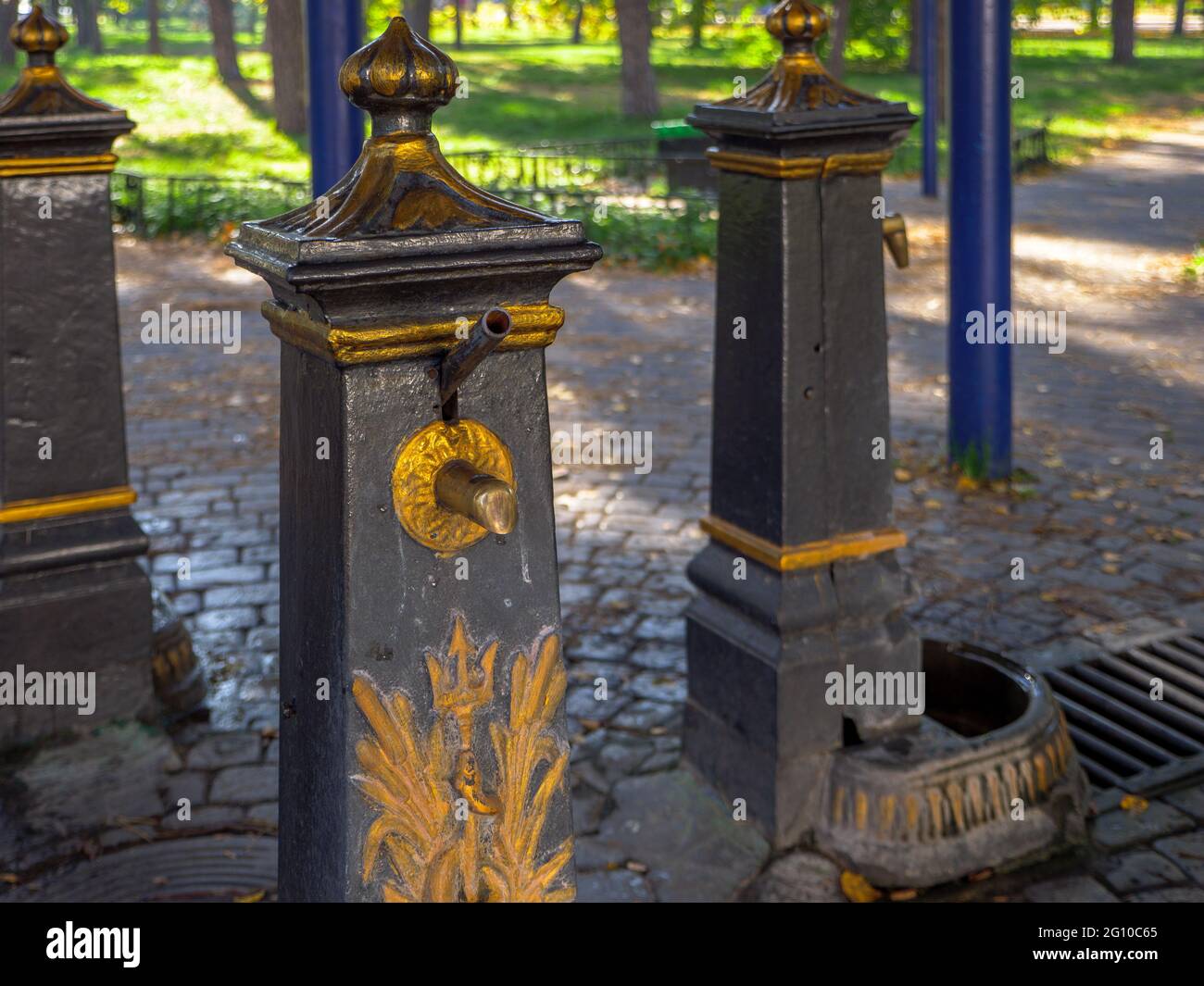 Altmodische öffentliche Metall-Handwasserpumpen mit goldener Dekoration, um sauberes Brunnenwasser für die Menschen zu erstellen, um es zu trinken und in Flaschen zu sammeln. Stockfoto