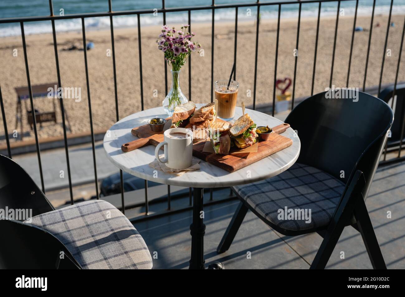 Hähnchen-Sandwich mit Eiskaffee und Blumendekoration auf der Terrasse des Cafés in der Nähe des Strandes am Morgen Stockfoto