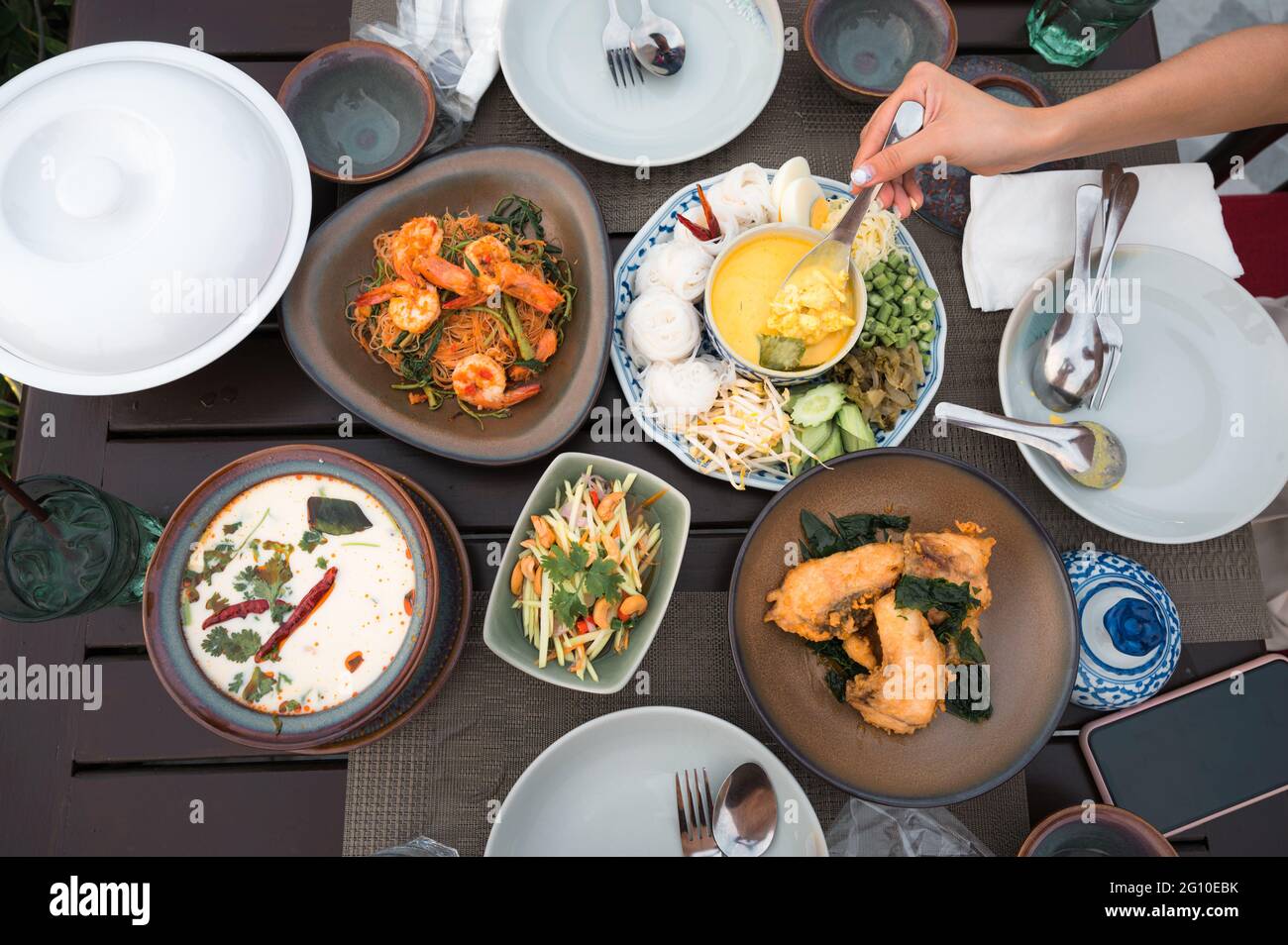 Draufsicht auf thailändisches Essen mit gesalzener Krabbe, Reisnudeln, gebratenem Seebarsch, gewürzter Mango, cremiger Hühnersuppe, Vermicelli Salat und Geschirr auf der TA Stockfoto