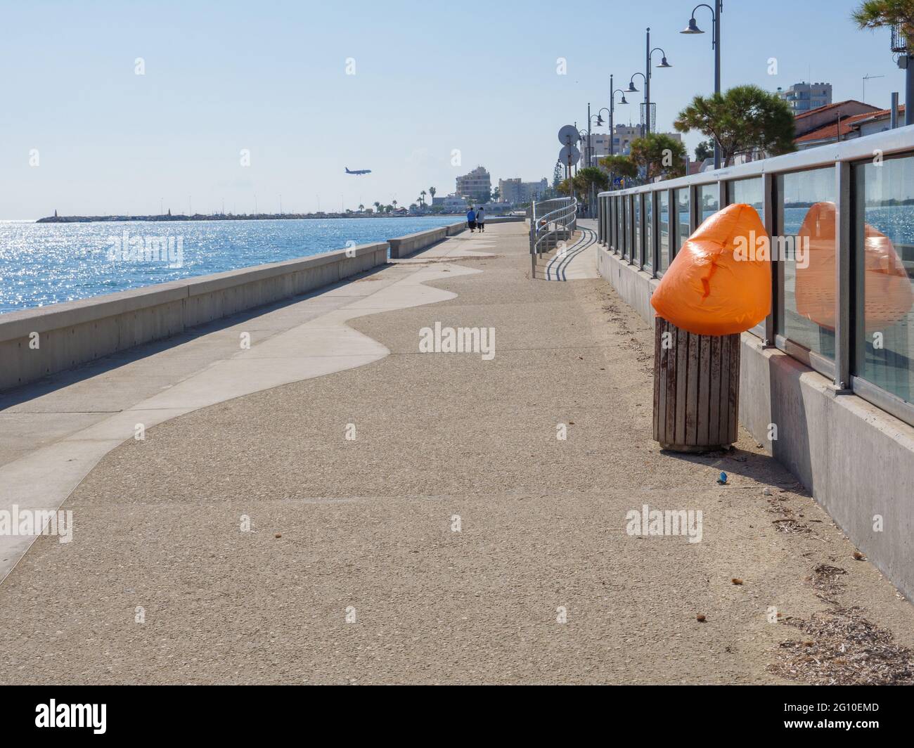 Lange leere Piale Pasha Betonpromenade entlang des blauen mittelmeers mit dem Flugzeug zum Flughafen Larnaca. Orangefarbener Plastikbeutel. Stockfoto