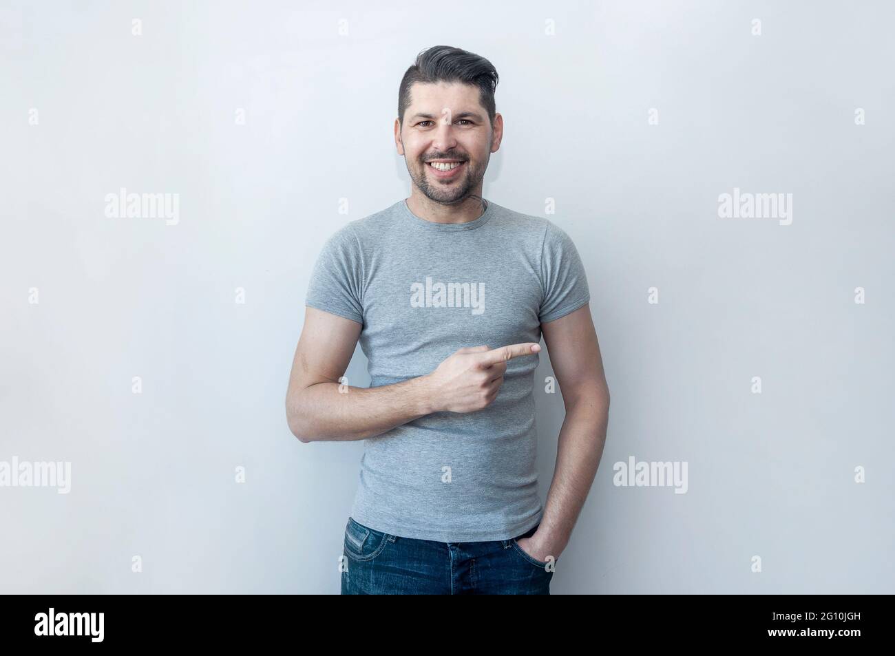 Hübscher Hipster lächelnder Mann zeigt mit Erstaunen weg, während er neues Angebot zeigt. Seht dort hin! Achtung weg, zeigt mit dem Daumen. Stockfoto
