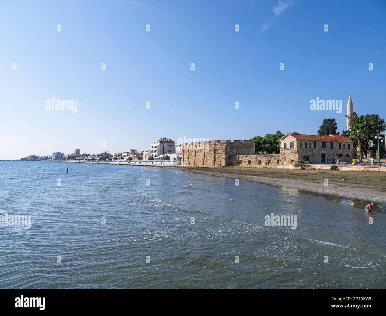 Blick vom Pier auf die alte Festung Larnaca, den Turm der Djami Kebir Moschee und den Strand mit vulkanischem Sand an einem sonnigen Tag in Zypern. Stockfoto