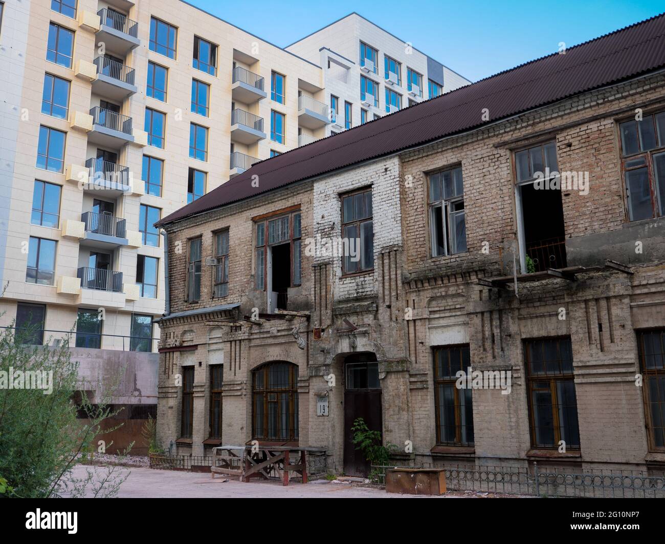 Das Äußere eines alten, halb ruinierten zweistöckigen, verlassenen Backsteingebäudes im Schatten eines neuen, frisch erbauten Hochhauses im Zentrum von Kiew, Ukraine. Stockfoto